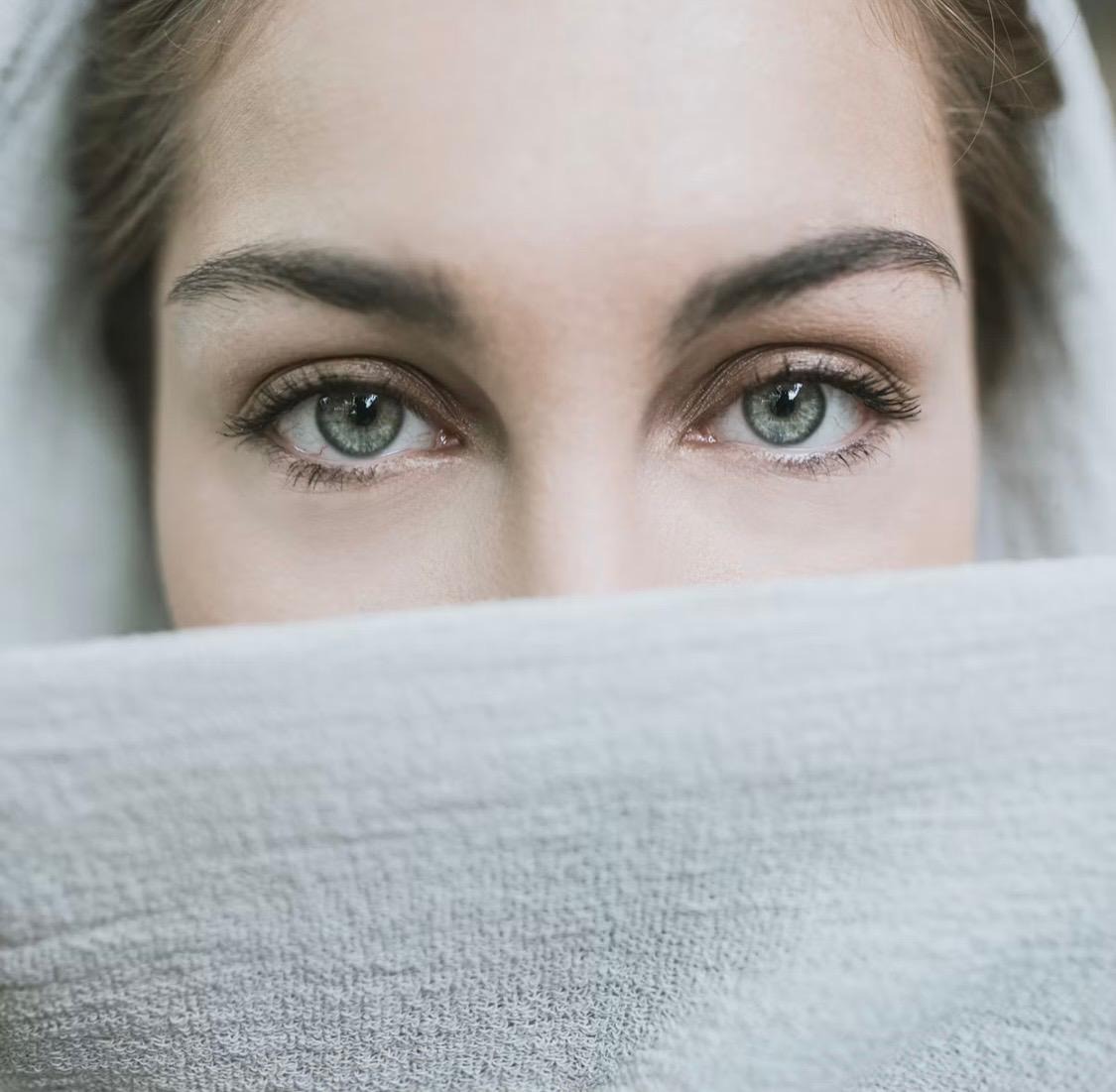 Eyes with defined brows peeking over a soft towel