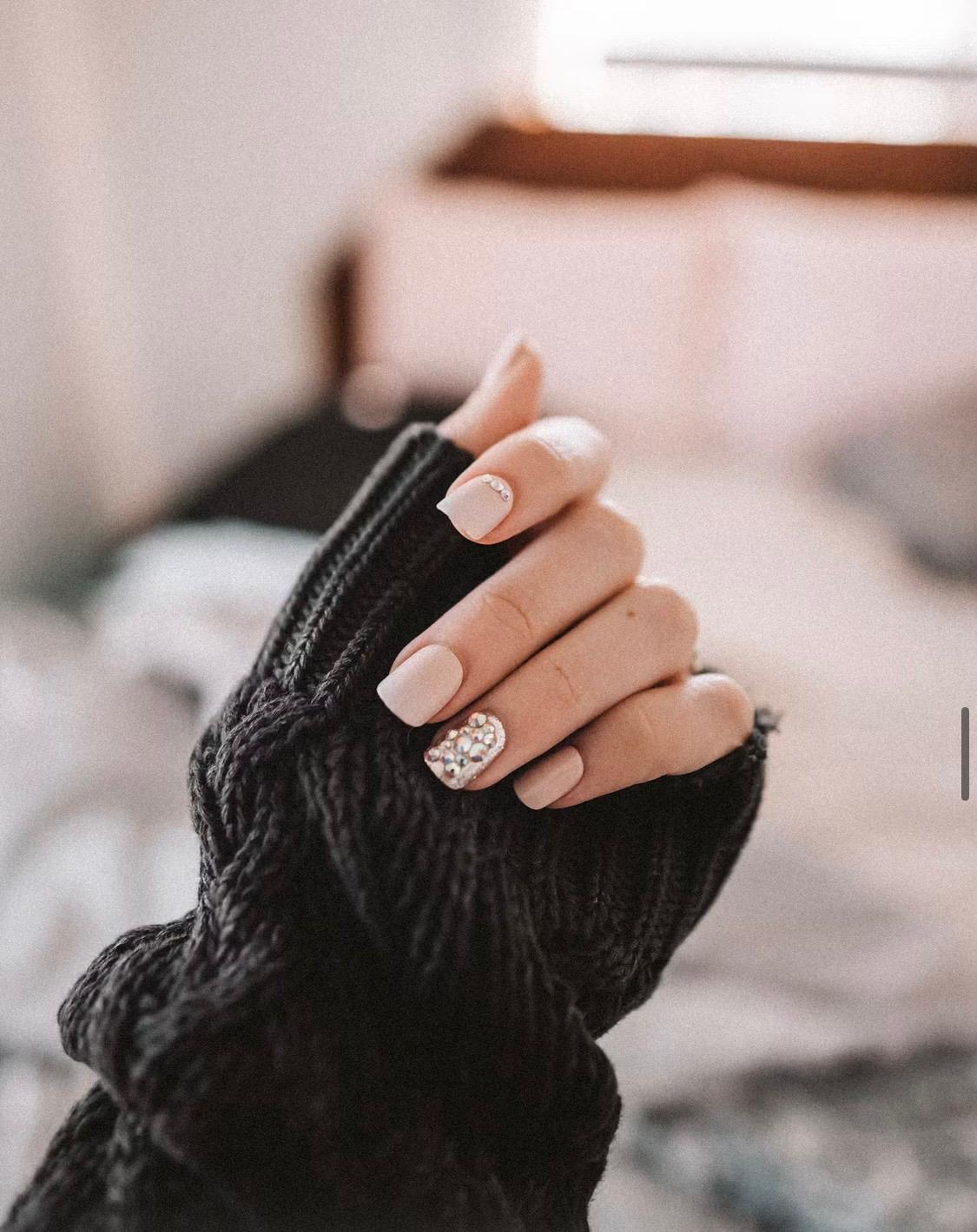 Nude gel nails with a crystal accent nail and black knit sleeve