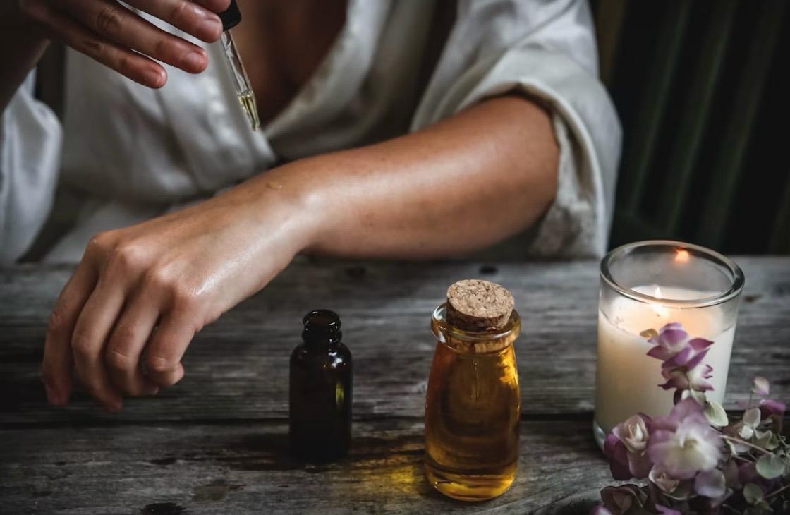 Aromatherapy oils beside a candle and dried flowers