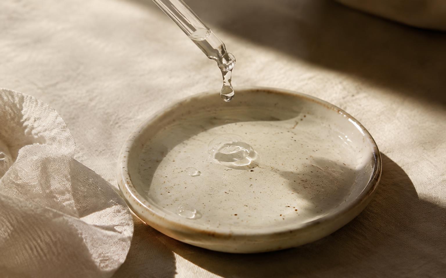 Drop of hydrating serum falling into a ceramic dish